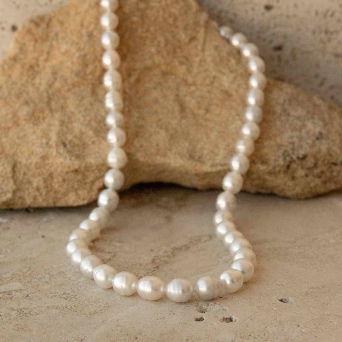 A strand of Australian South Sea Circle pearls arranged in a loop on a textured beige stone surface with a larger tan rock behind it.