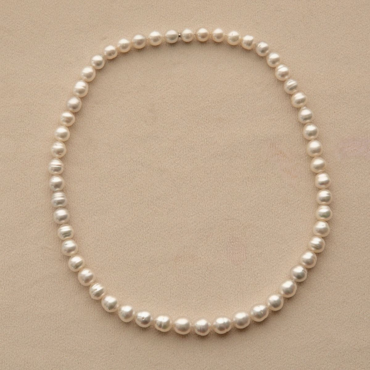 A classic Australian South Sea pearl strand necklace arranged in a neat circle on a textured beige background.