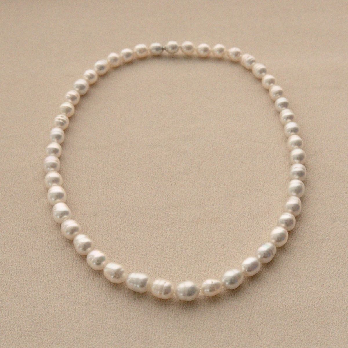 A single pearl strand necklace of Australian South Sea pearls arranged in a circle on a textured beige background.