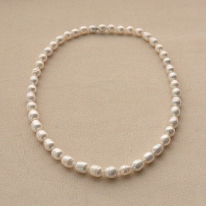 A single pearl strand necklace of Australian South Sea pearls arranged in a circle on a textured beige background.
