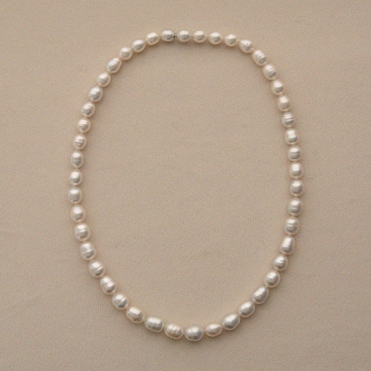 A strand of Australian South Sea pearls arranged in an oval shape on a light beige textured background.