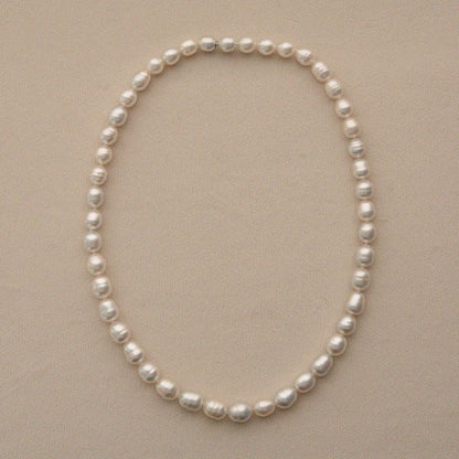 A strand of Australian South Sea pearls arranged in an oval shape on a light beige textured background.