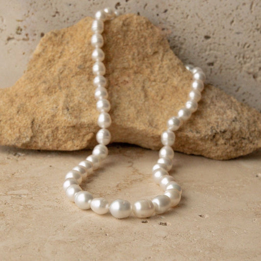 A strand of Australian South Sea pearls draped over a natural tan rock on a textured stone surface.