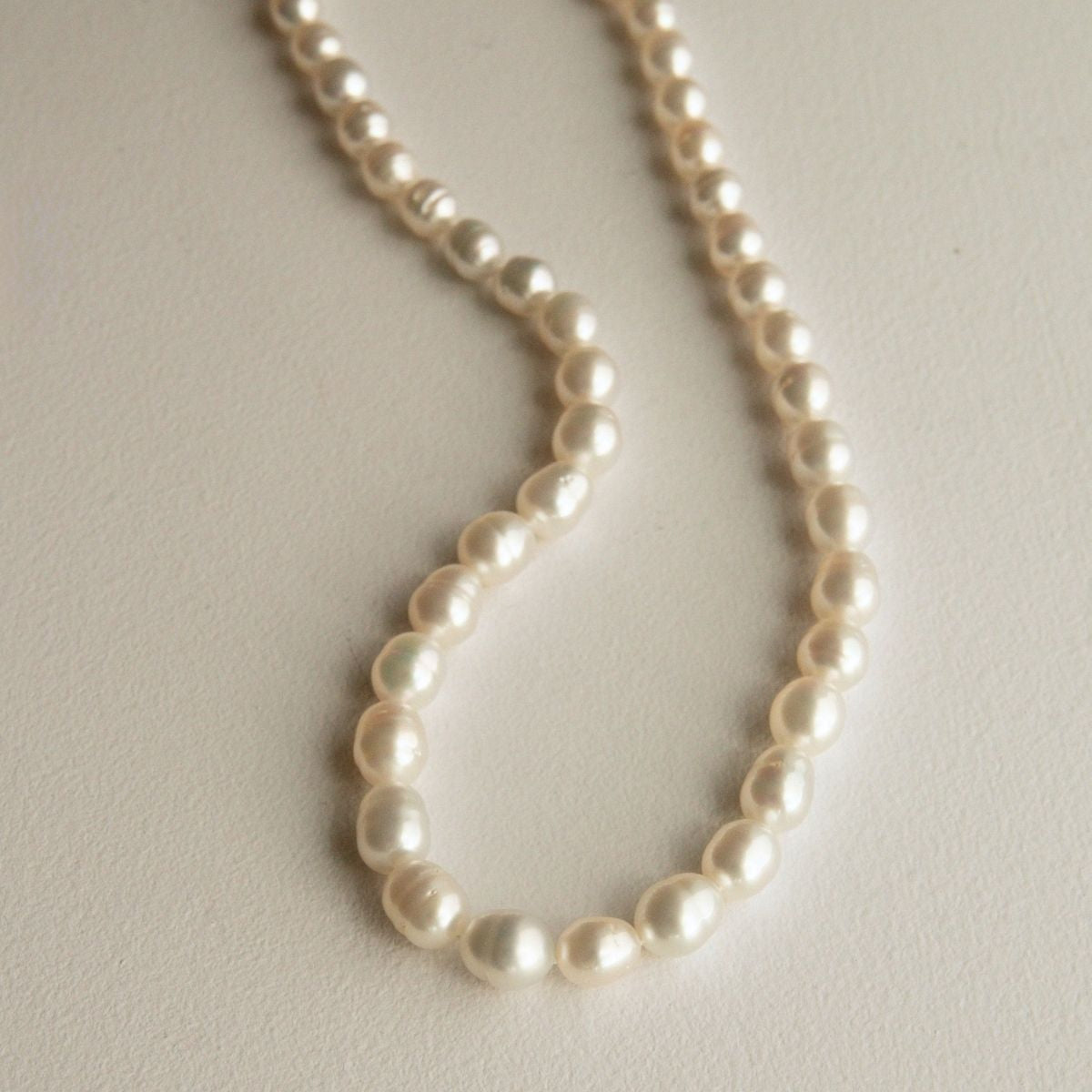 A strand of circle shaped Australian South Sea pearls draped in a loop on a light beige textured surface.
