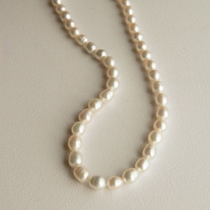 A strand of circle shaped Australian South Sea pearls draped in a loop on a light beige textured surface.