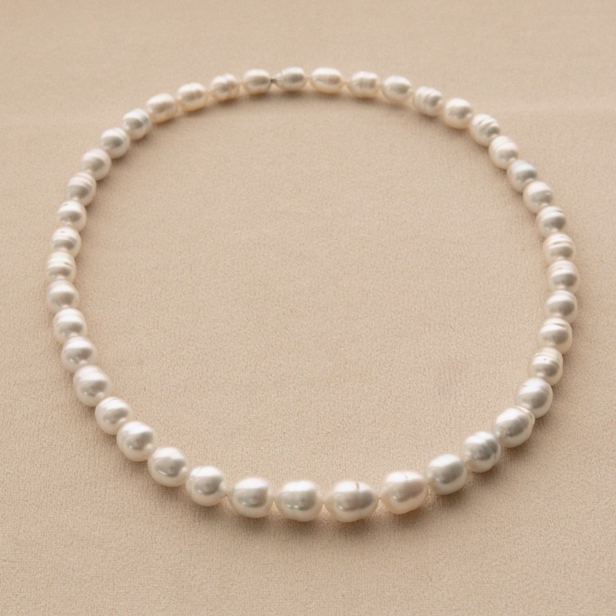A single strand of Australian South Sea pearls arranged in a circle on a textured beige background.