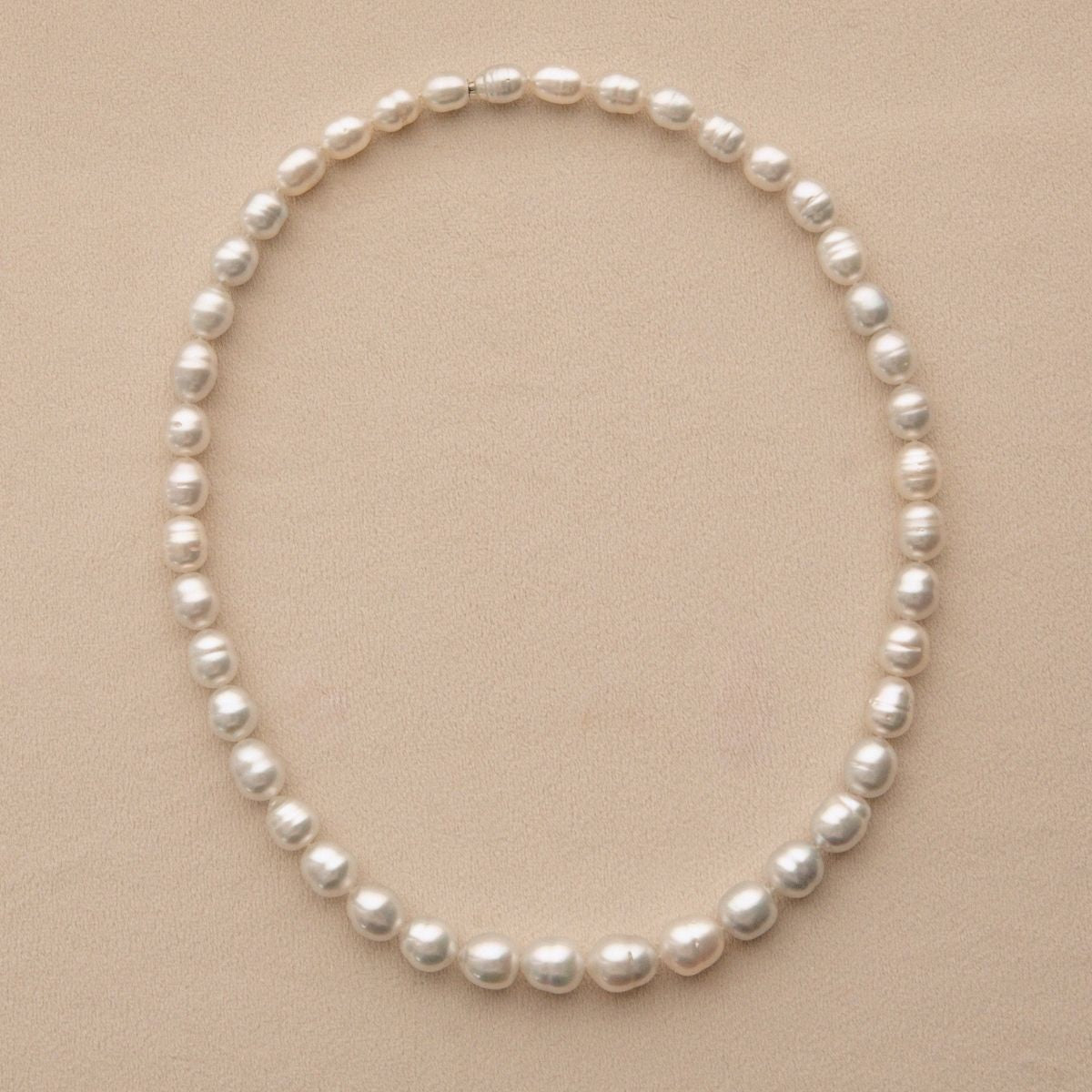 A strand necklace featuring Australian South Sea pearls arranged in a neat circle on a textured beige background.