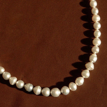 A strand of circle shape Australian South Sea pearls arranged in a curve on a textured dark brown background.