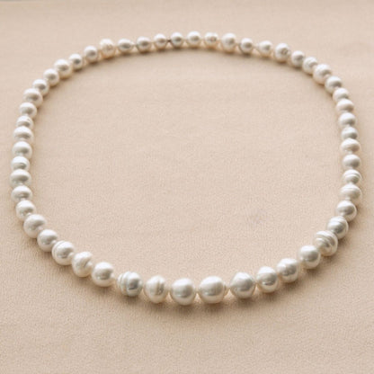 A single strand of Australian South Sea pearls arranged in a circle on a textured beige background.