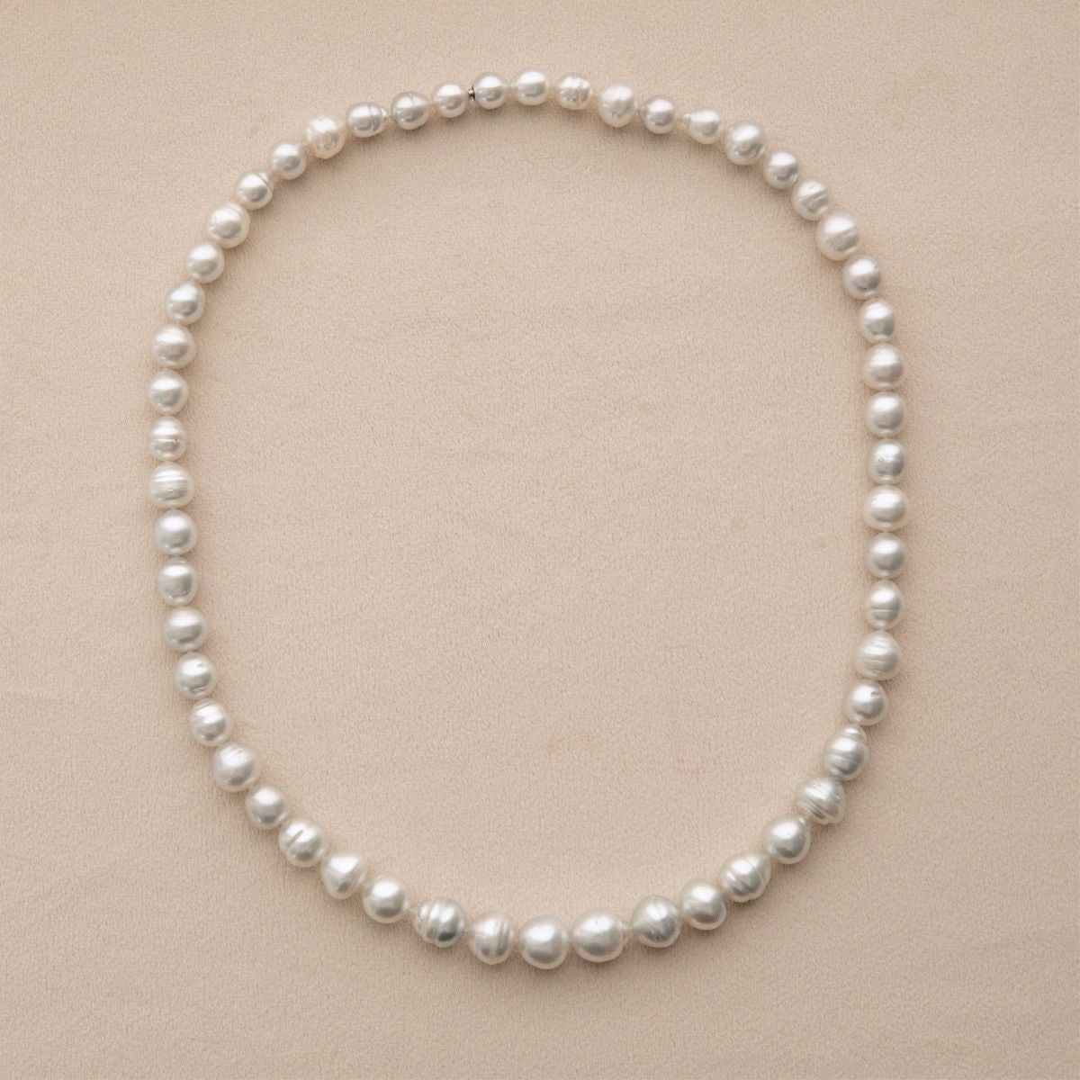 A strand of Australian South Sea pearls arranged in a circle on a light beige textured background.