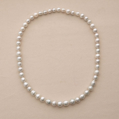 A strand of Australian South Sea pearls arranged in a circle on a light beige textured background.