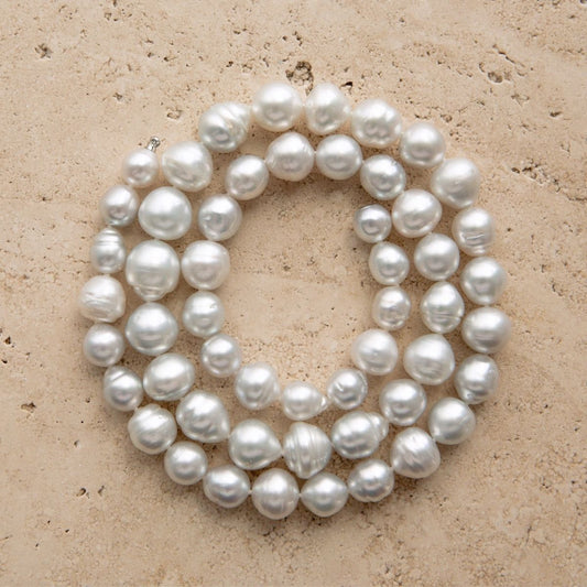 A strand of Australian South Sea pearls arranged in a loose circle on a textured beige stone surface.