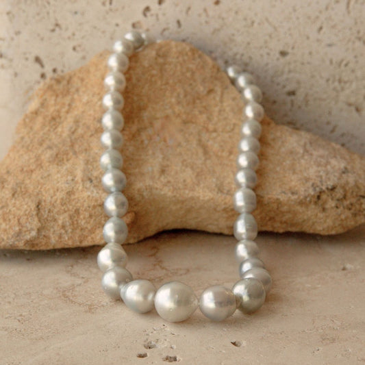 A pearl strand necklace of irregular shape Australian South Sea pearls draped over a tan rock on a textured beige stone surface.