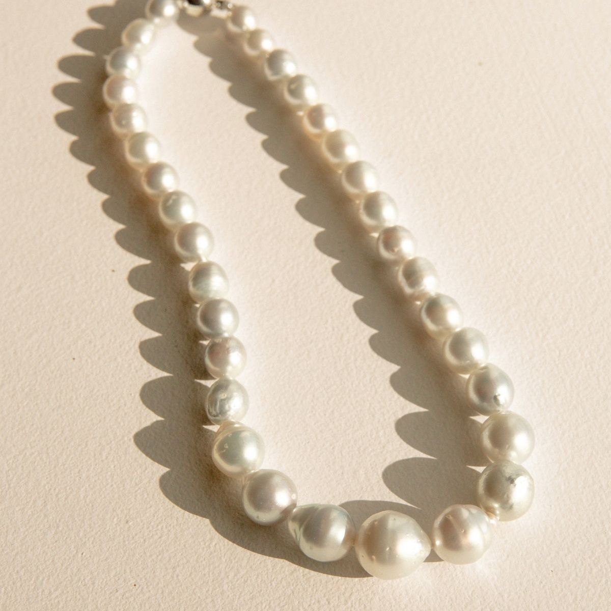 A strand of irregular silver-blue Australian South Sea pearls arranged in a loop on a textured beige surface, casting soft shadows.