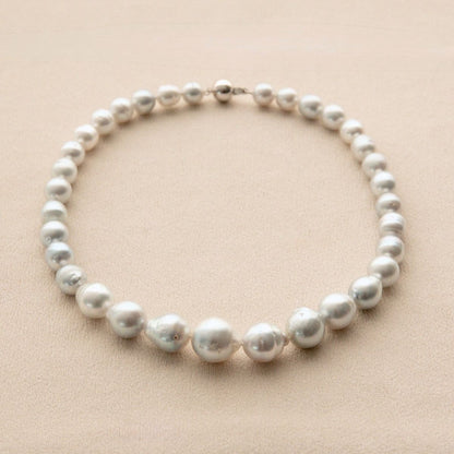 A strand of irregularly shape Australian South Sea pearls arranged in a circle on a light beige textured background.