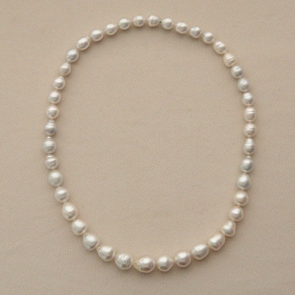 A pearl strand of circle shape Australian South Sea pearls arranged in an oval shape on a light beige textured background.