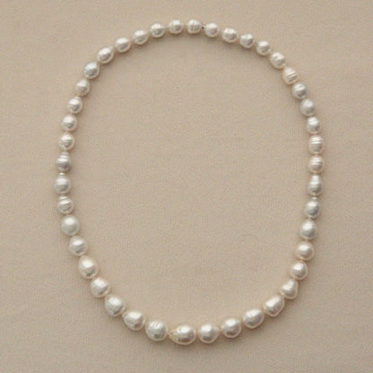 A pearl strand of circle shape Australian South Sea pearls arranged in an oval shape on a light beige textured background.