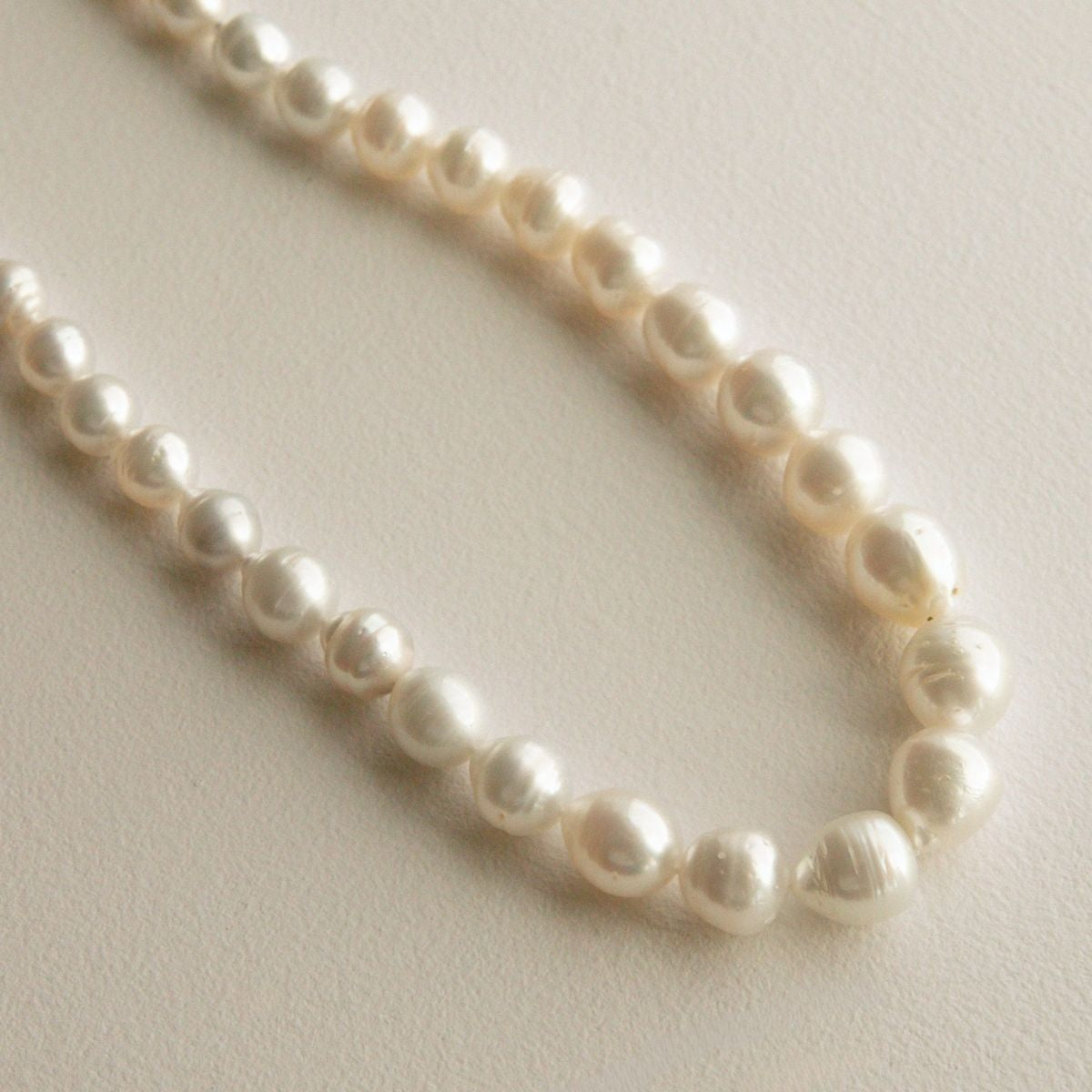 A strand of circle shape Australian South Sea pearls arranged in a loose curve on a light beige textured background.