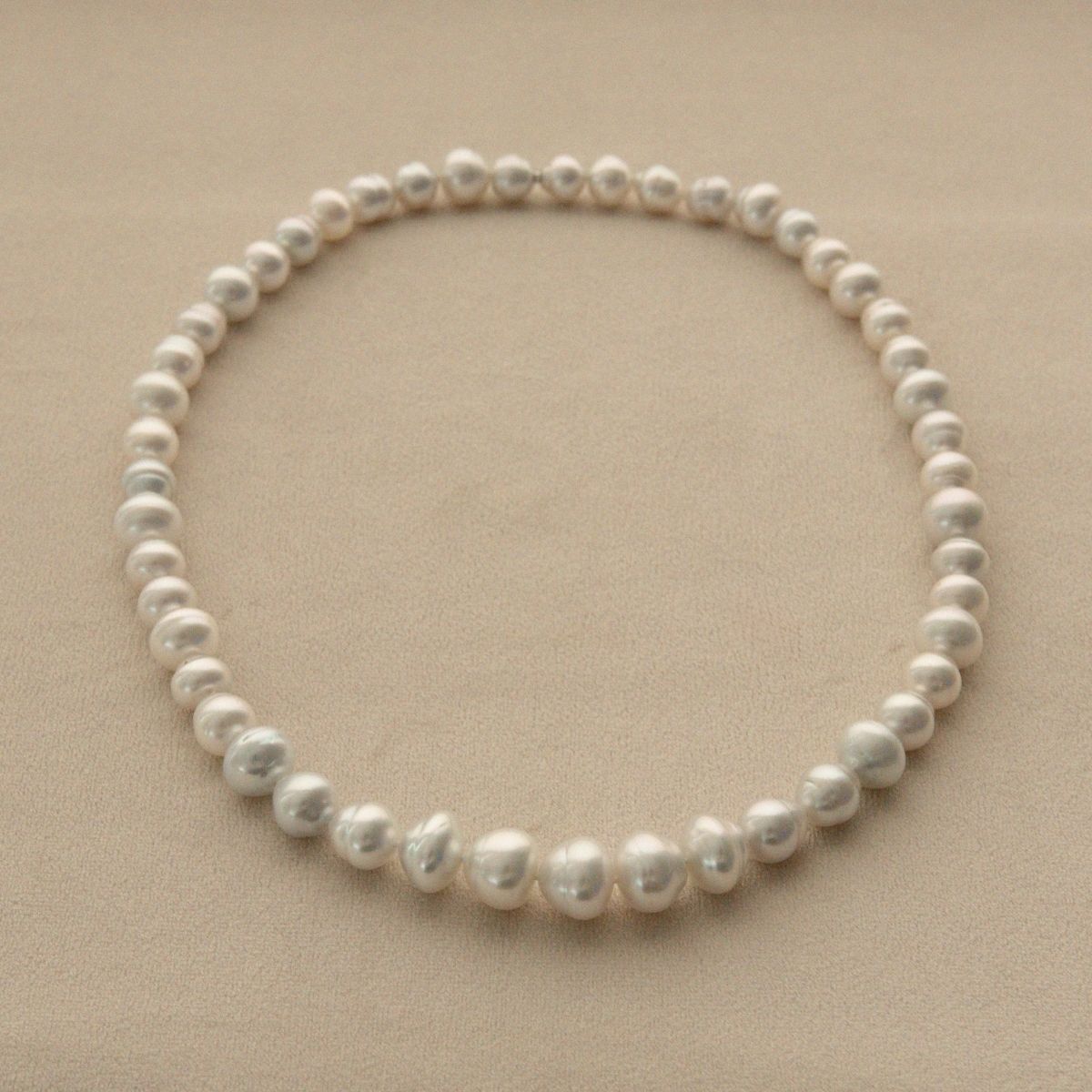 A strand of Australian South Sea pearls arranged in a circle on a neutral beige background.