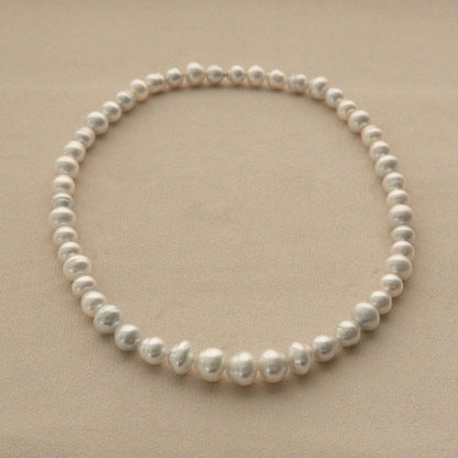 A strand of Australian South Sea pearls arranged in a circle on a neutral beige background.
