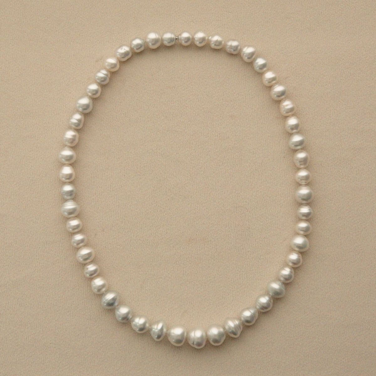 A strand of Australian South Sea pearls arranged in an oval shape on a light beige background.