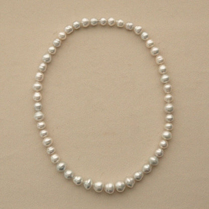 A strand of Australian South Sea pearls arranged in an oval shape on a light beige background.
