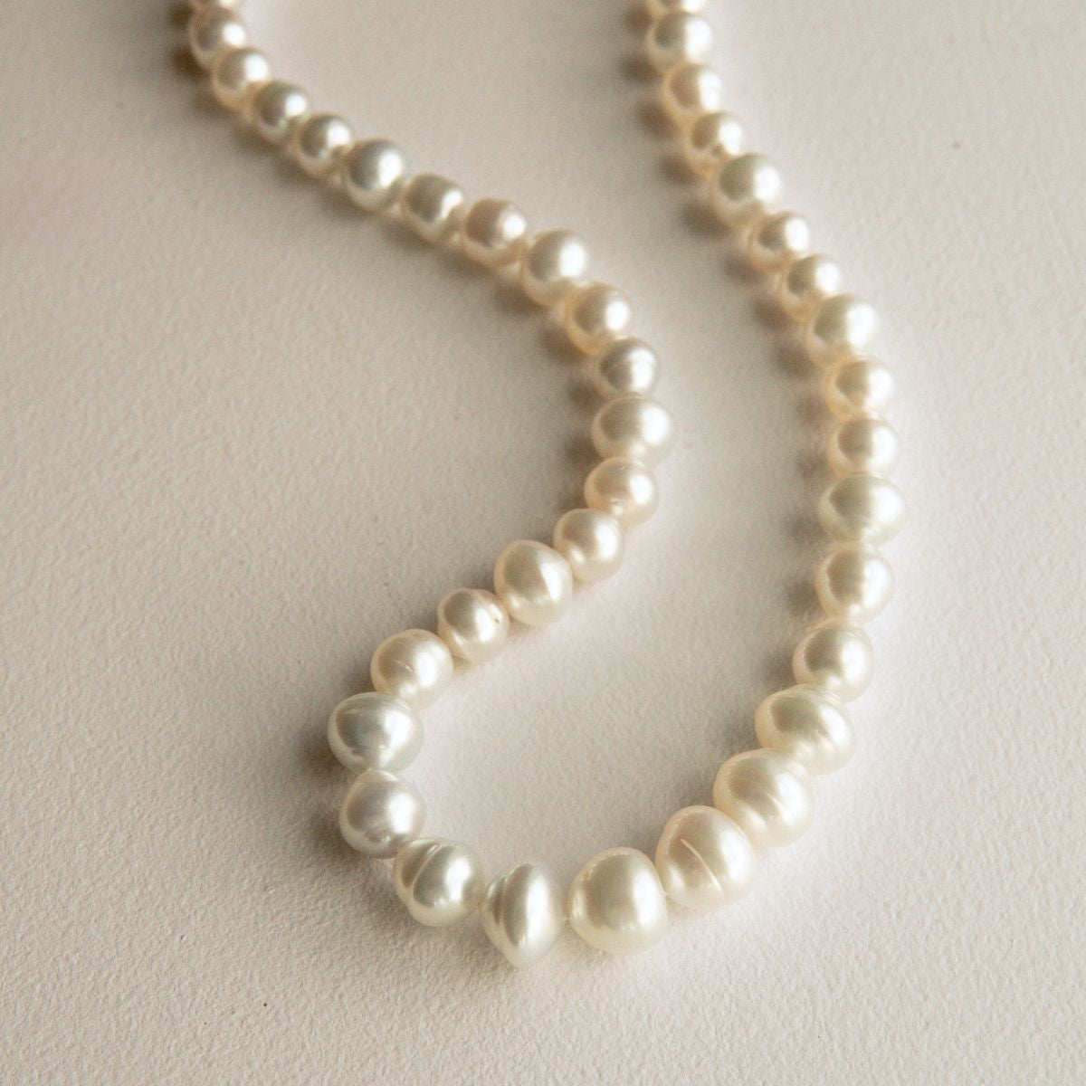 A strand of Australian South Sea pearls draped in a loose curve on a light beige textured surface.