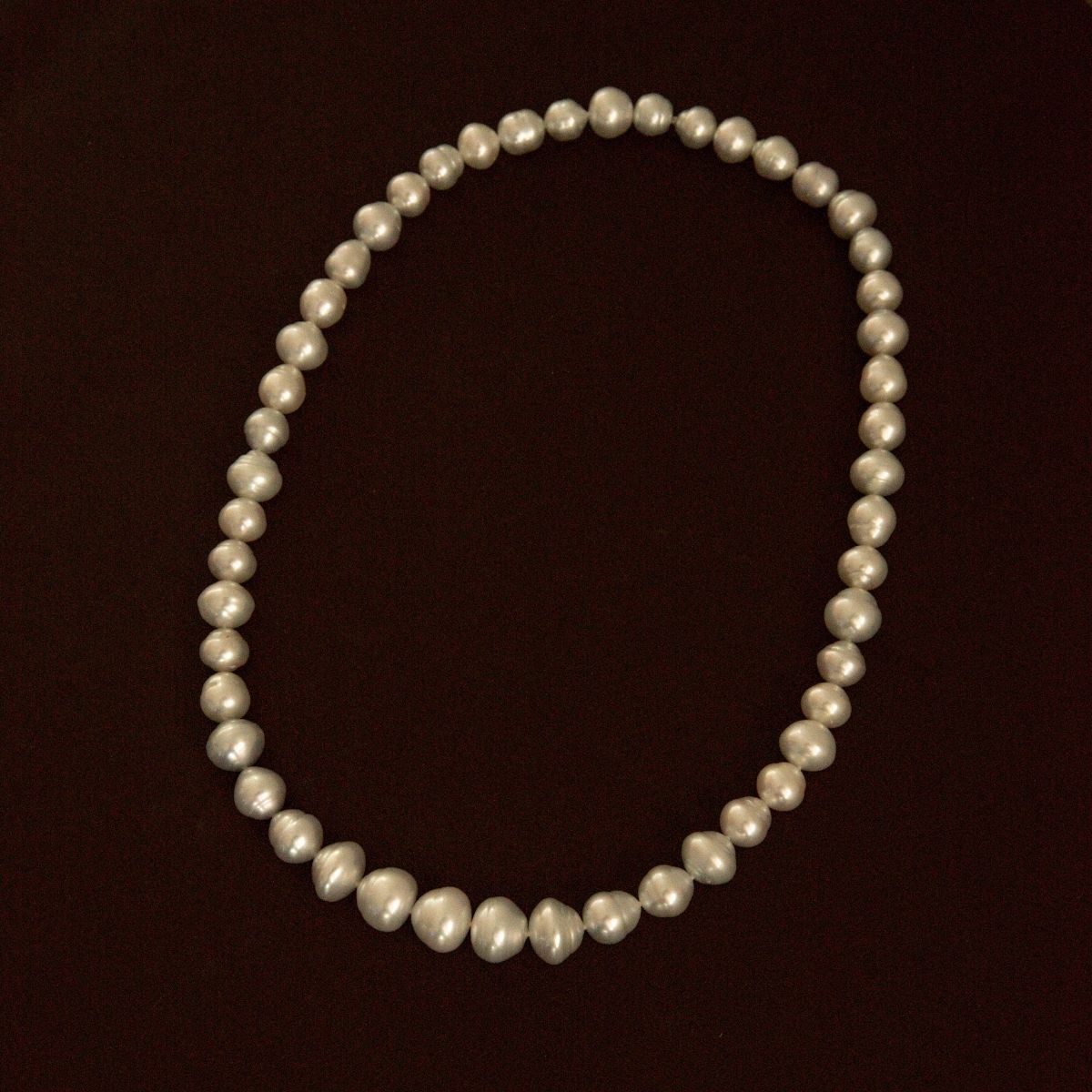 A strand of Australian South Sea pearls arranged in an oval shape against a solid dark brown background.