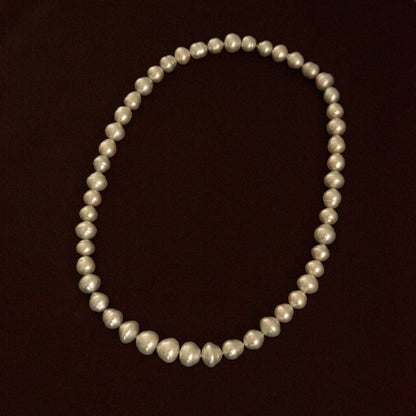 A strand of Australian South Sea pearls arranged in an oval shape against a solid dark brown background.