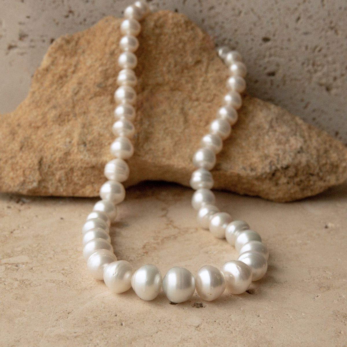 A strand of circle Australian South Sea pearls draped over a tan rock on a textured beige stone surface.