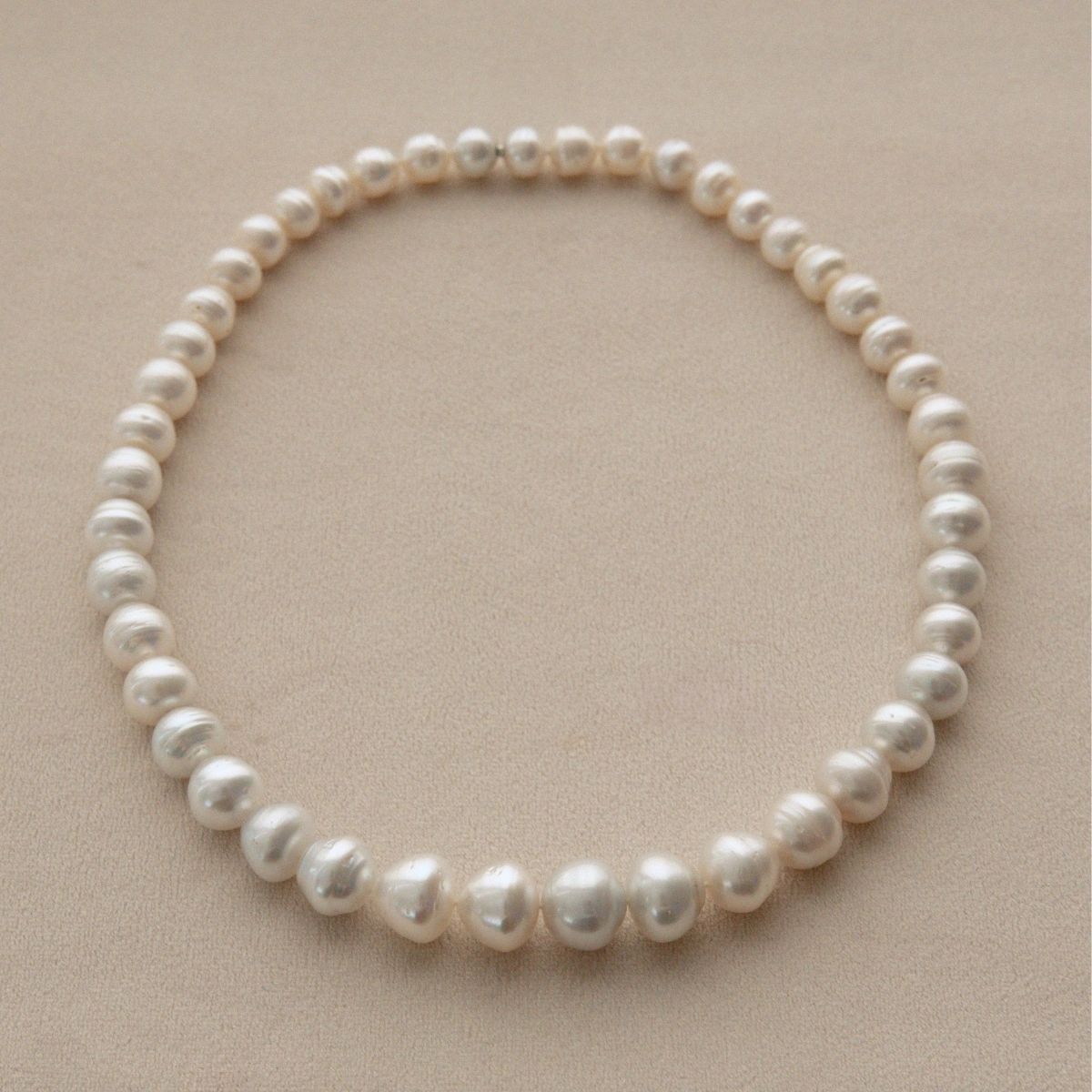 A strand of circle shape Australian South Sea pearls arranged in a circle on a neutral beige background.