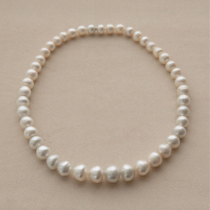 A strand of circle shape Australian South Sea pearls arranged in a circle on a neutral beige background.