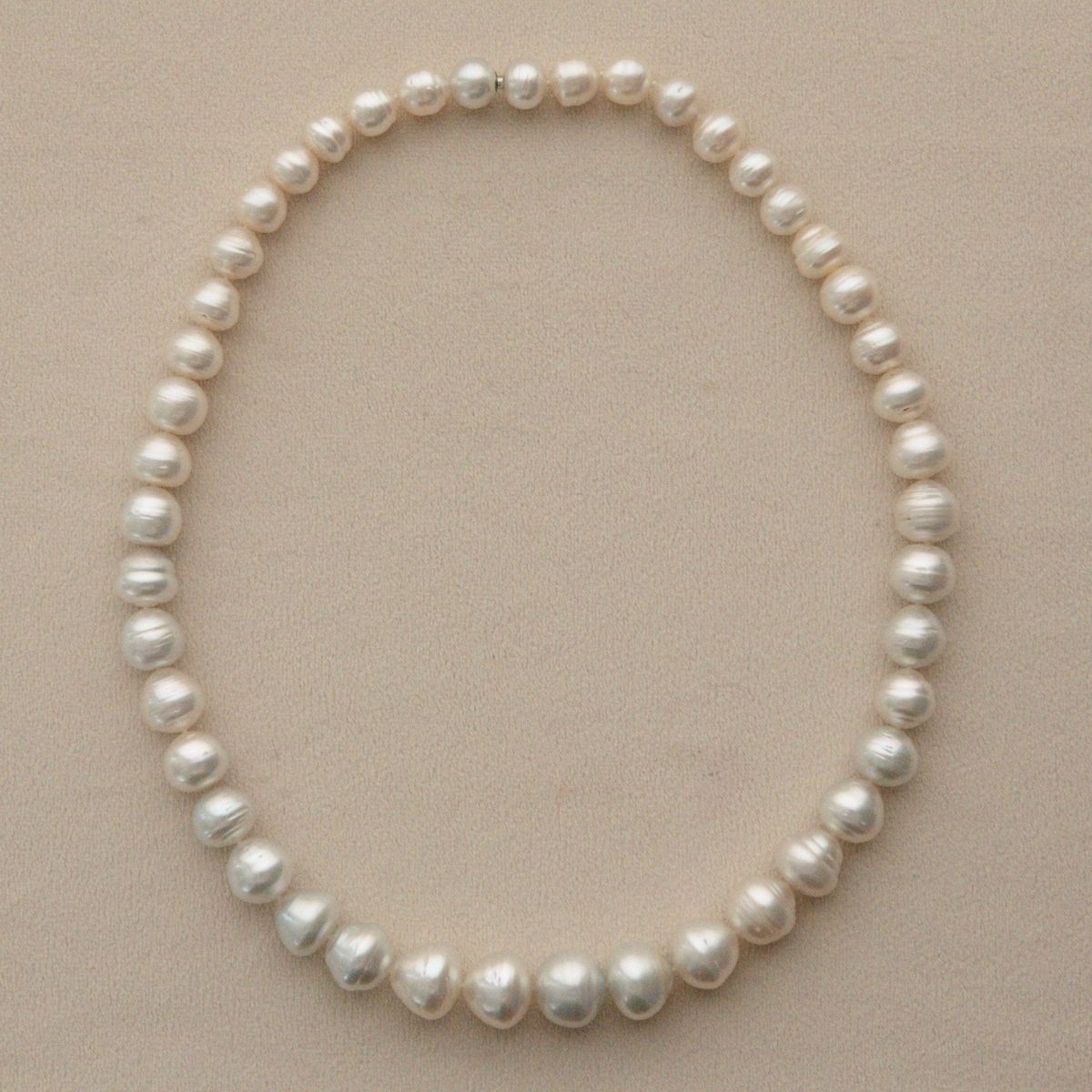 A graduated strand of Australian South Sea pearls arranged in a circle on a light beige textured background.