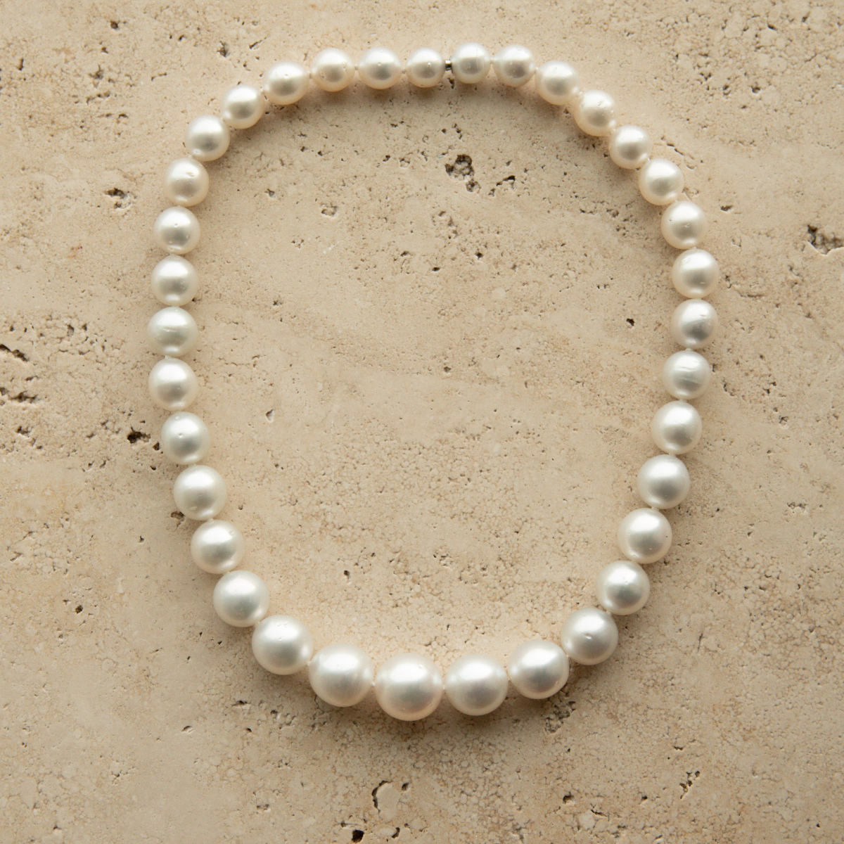 Round pearl strand necklace on a textured beige surface