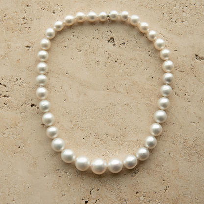 Round pearl strand necklace on a textured beige surface