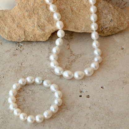 A white Australian South Sea pearl necklace and matching pearl bracelet arranged on a light stone surface with a larger tan rock prop in the background.