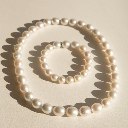 A strand of white Australia South Sea pearls from Cygnet Bay Pearl Farm in a circle on a warm cream background, with a matching bracelet nested inside. The beads are photographed in direct sunlight, casting sharp shadows.