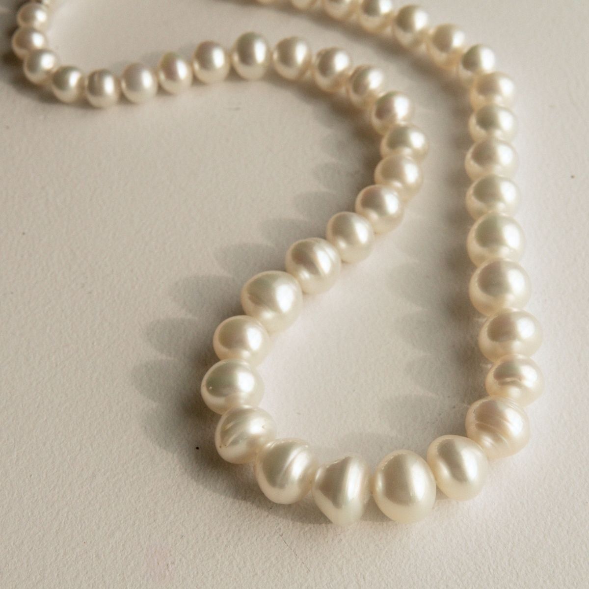 A strand of Australian South Sea pearls draped in a loop on a light beige textured surface.