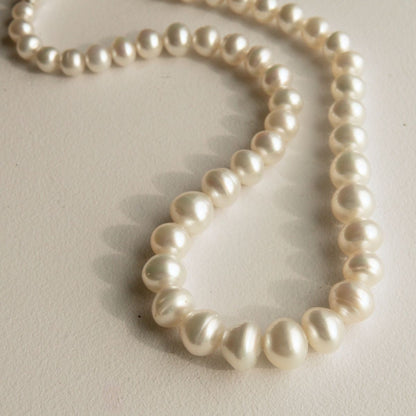 A strand of Australian South Sea pearls draped in a loop on a light beige textured surface.
