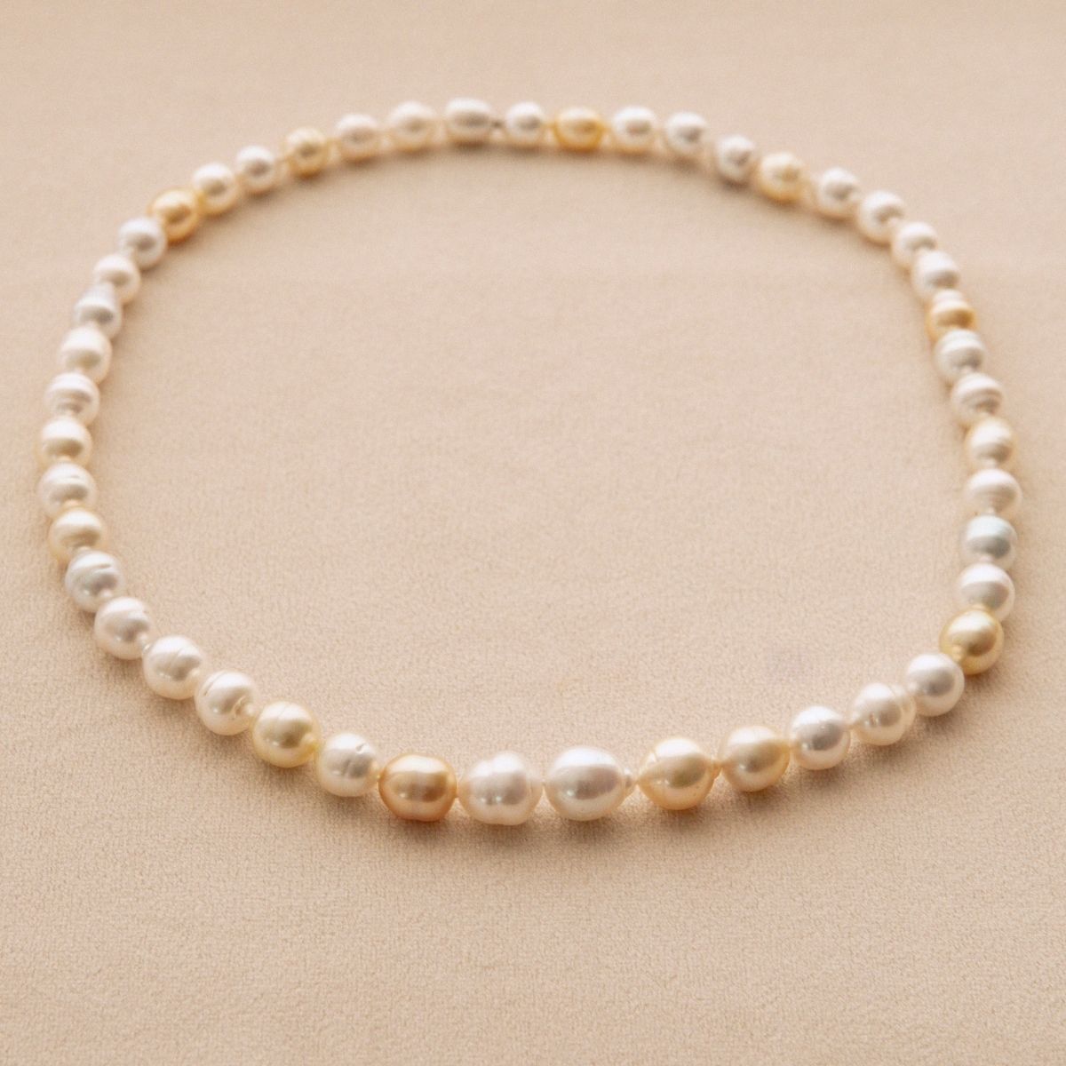 A strand of Australian South Sea pearls arranged in a circle on a textured beige background.