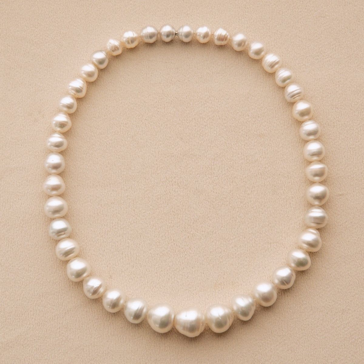 A strand of Cygnet Bay grown Australian South Sea pearls arranged in a circle on a textured beige background.