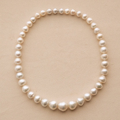 A strand of Cygnet Bay grown Australian South Sea pearls arranged in a circle on a textured beige background.