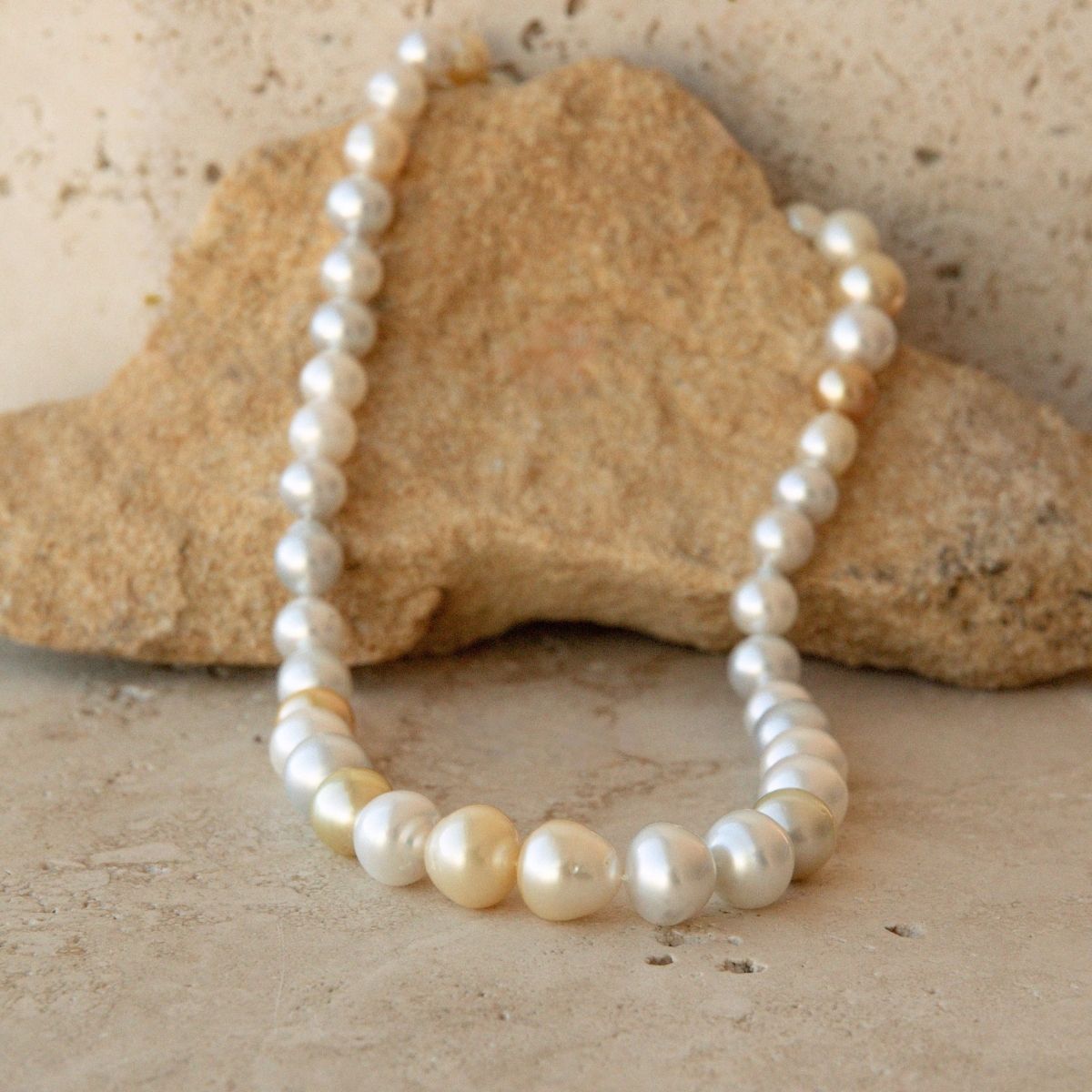 A pearl strand of Australian South Sea pearls draped over a tan stone on a textured beige surface.