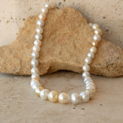 A pearl strand of Australian South Sea pearls draped over a tan stone on a textured beige surface.