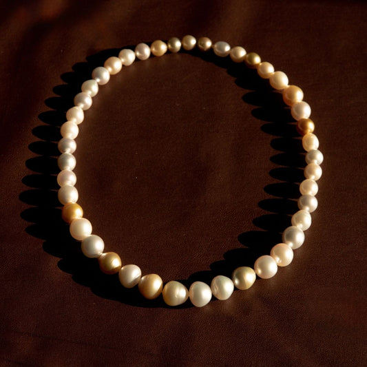 A strand of mixed shape Australian South Sea pearls arranged in a circle on a dark brown background, casting soft shadows.