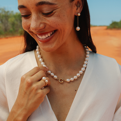 Woman wearing a pearl necklace and earrings outdoors with a clear sky.