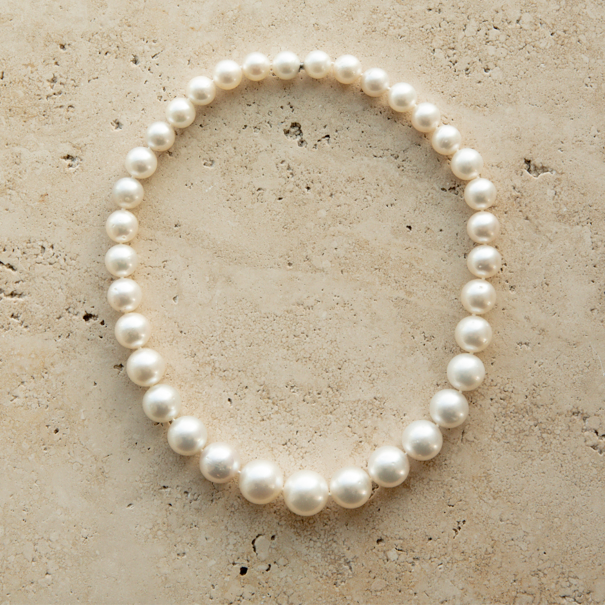 Pearl strand necklace on a textured beige surface