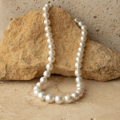 A strand of Australian South Sea pearls draped over a tan rock on a textured beige stone surface.