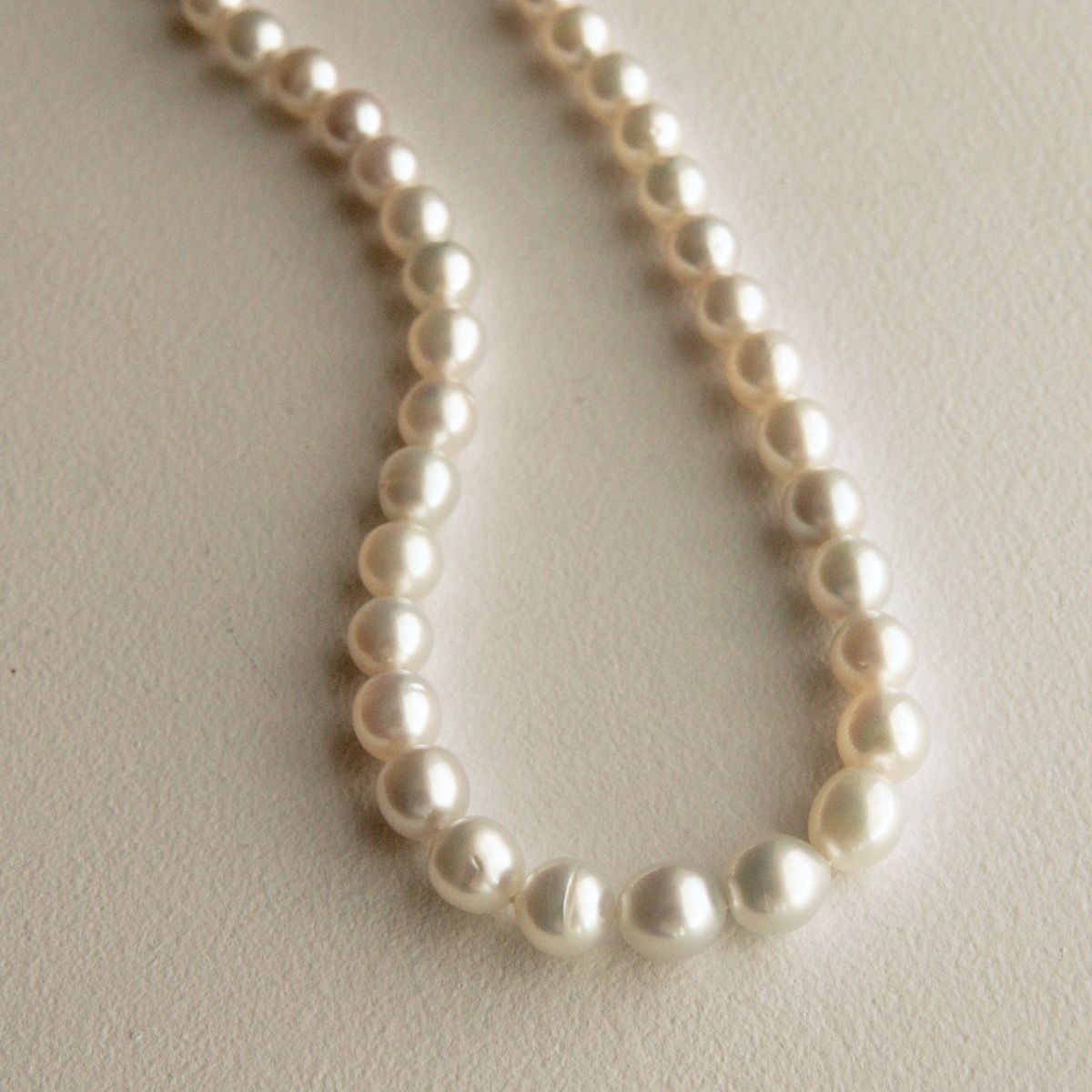 An Australian South Sea pearl strand necklace featuring Cygnet Bay grown pearls draped in a U-shape on a textured off-white background.