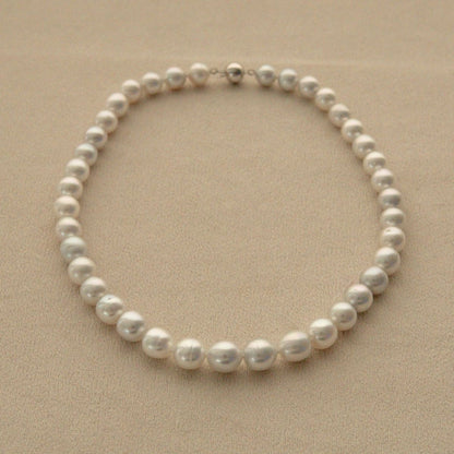 A strand of semi drop shape Australian South Sea pearls arranged in a circle on a textured beige background, featuring a small silver clasp at the top.